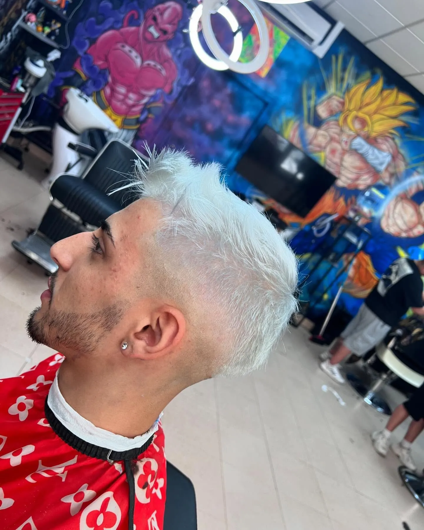 Cliente con el pelo platinado frente al mural de Dragon Ball de la barbería